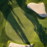 Vogelperspektive auf einen grünen Golfplatz mit Bäumen und zwei ovalen Sandbereichen