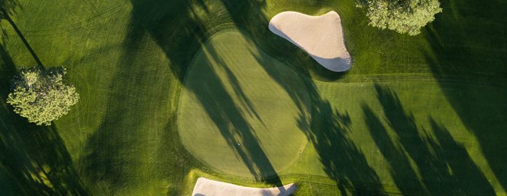 Vogelperspektive auf einen grünen Golfplatz mit Bäumen und zwei ovalen Sandbereichen